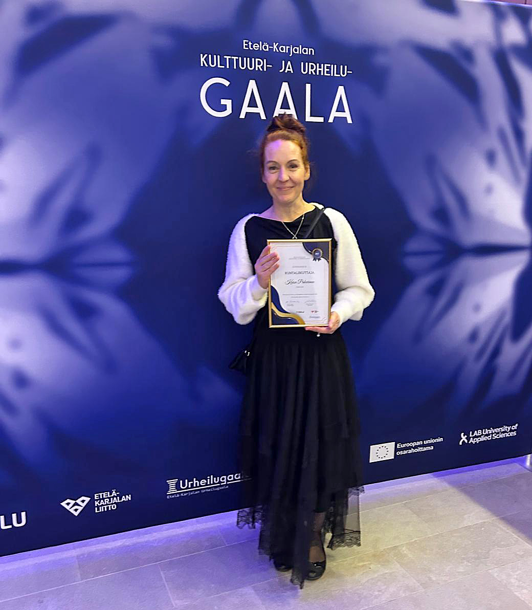 Nainen mustassa mekossa seisoo ja pitelee kädessään palkintodiplomia.