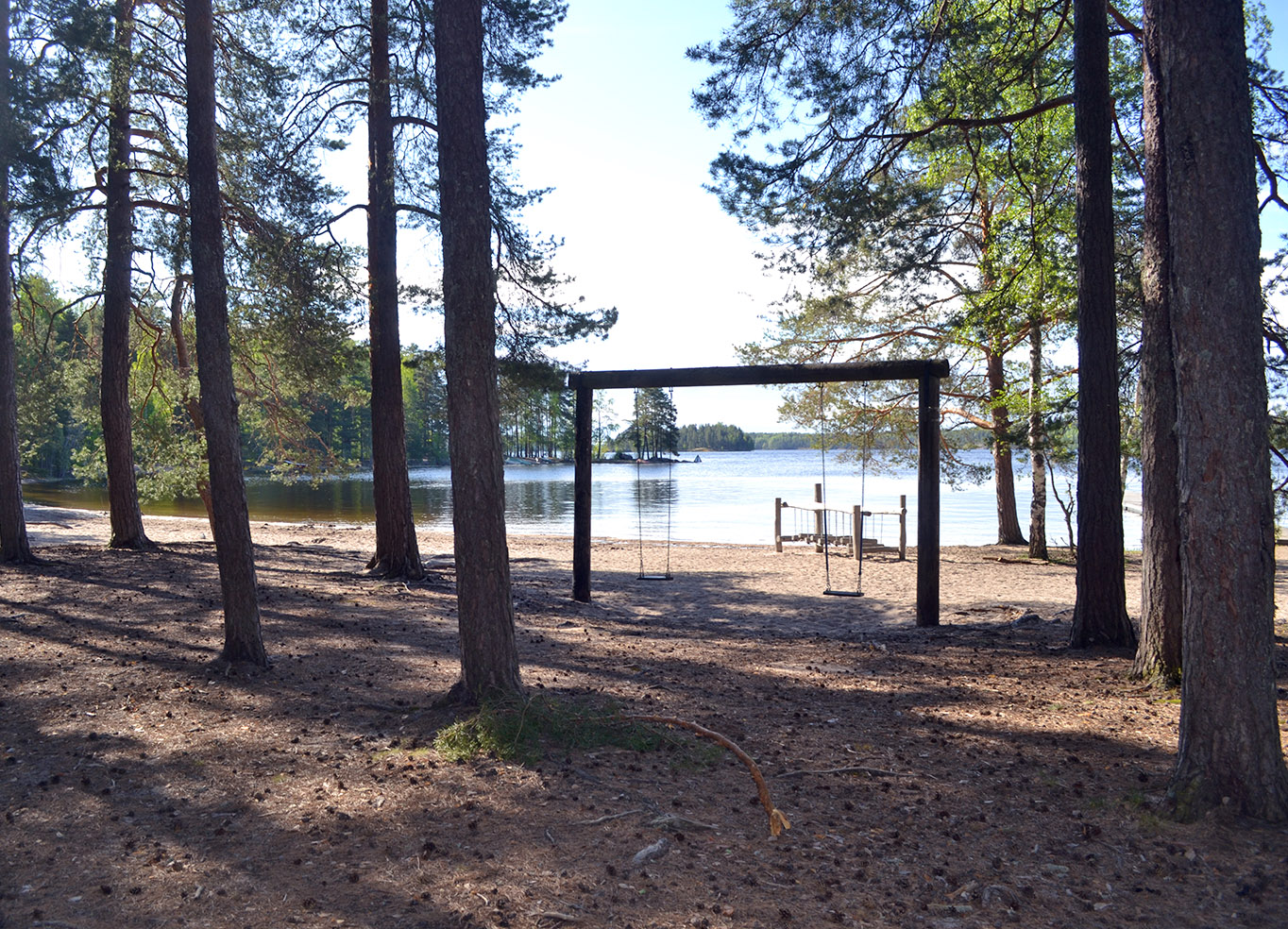 Hiekkaranta, puita ja kaksi keinua.