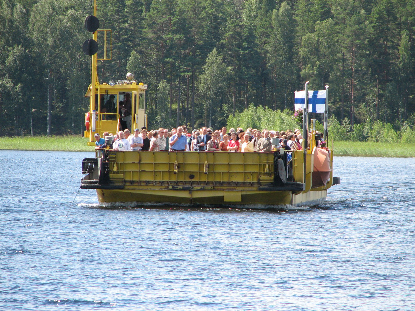 Keltainen lossi vesillä. Lossi on täynnä ihmisiä.